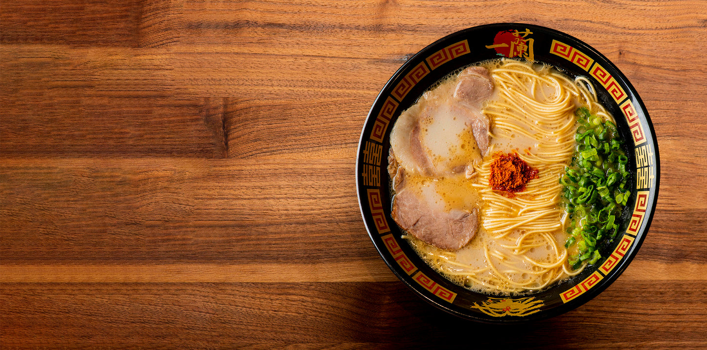 Wooden table with a bowl of ICHIRAN's Classic Tonkotsu Ramen on the right